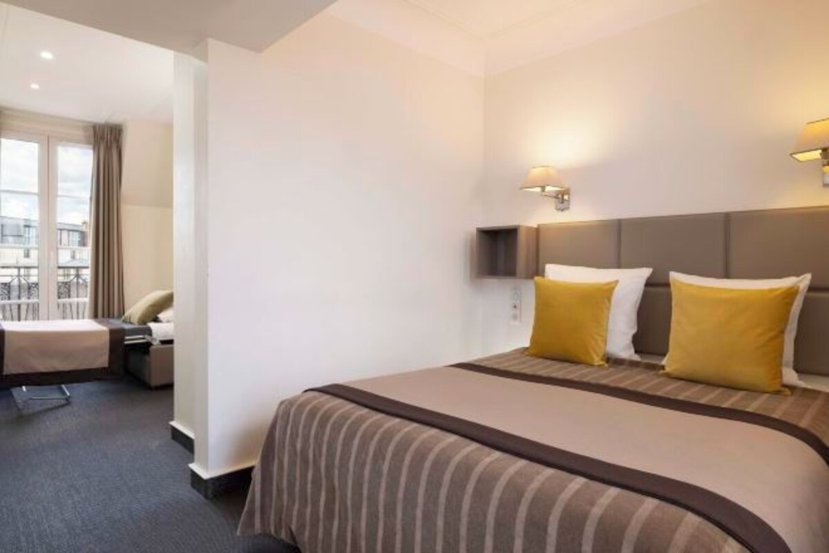 A hotel room with a large bed, two bedside lamps, and a view of the outside.