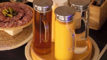 Un plateau en bois contenant trois verres en verre remplis de différentes boissons, une planche en bois avec des tranches de viande et des cornichons, et un porte-ustensiles en bois en arrière-plan.