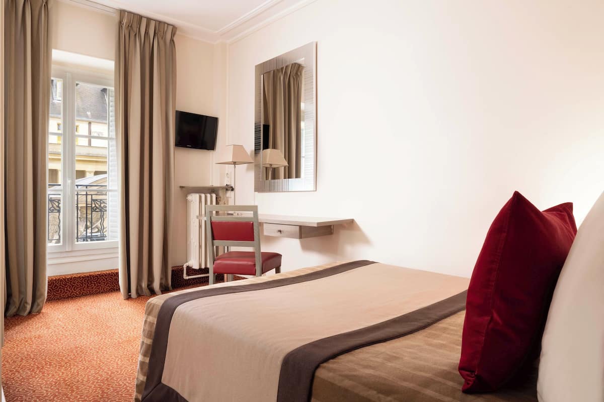 A hotel room with a bed, a desk, a chair, a TV, and a window with curtains.