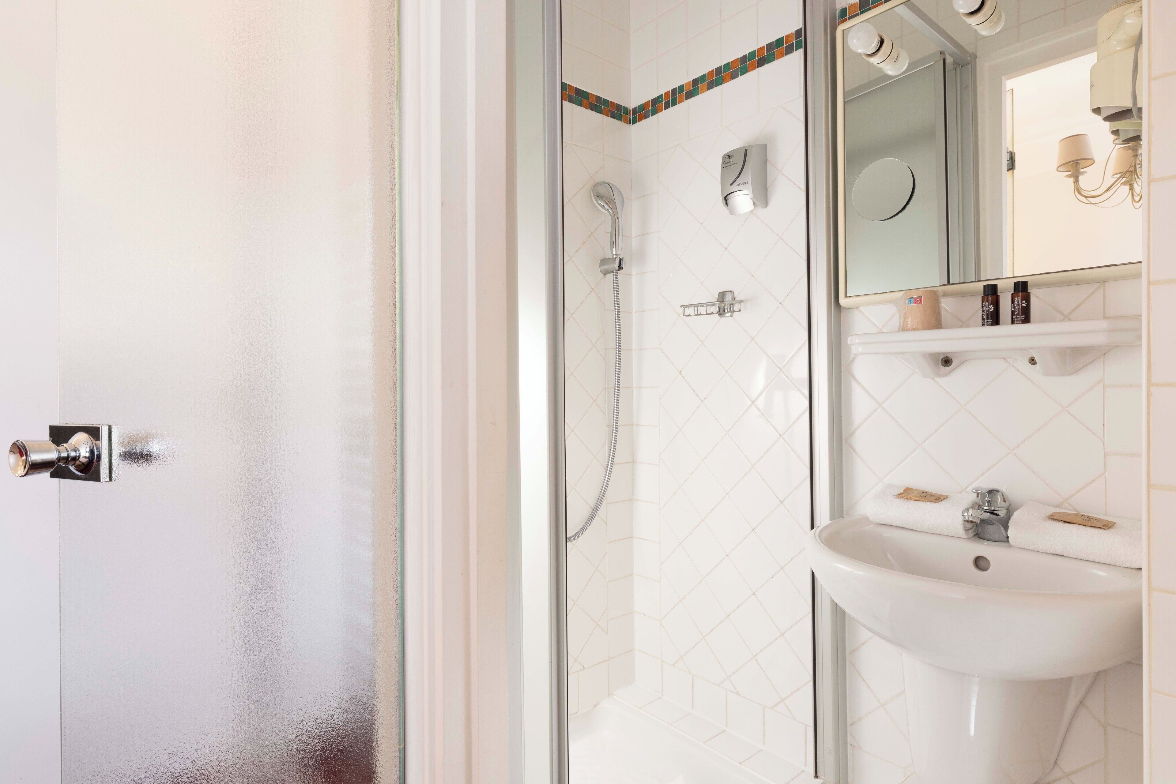 A bathroom with a glass shower enclosure, a sink with a mirror above it, and toiletries on the sink's edge.