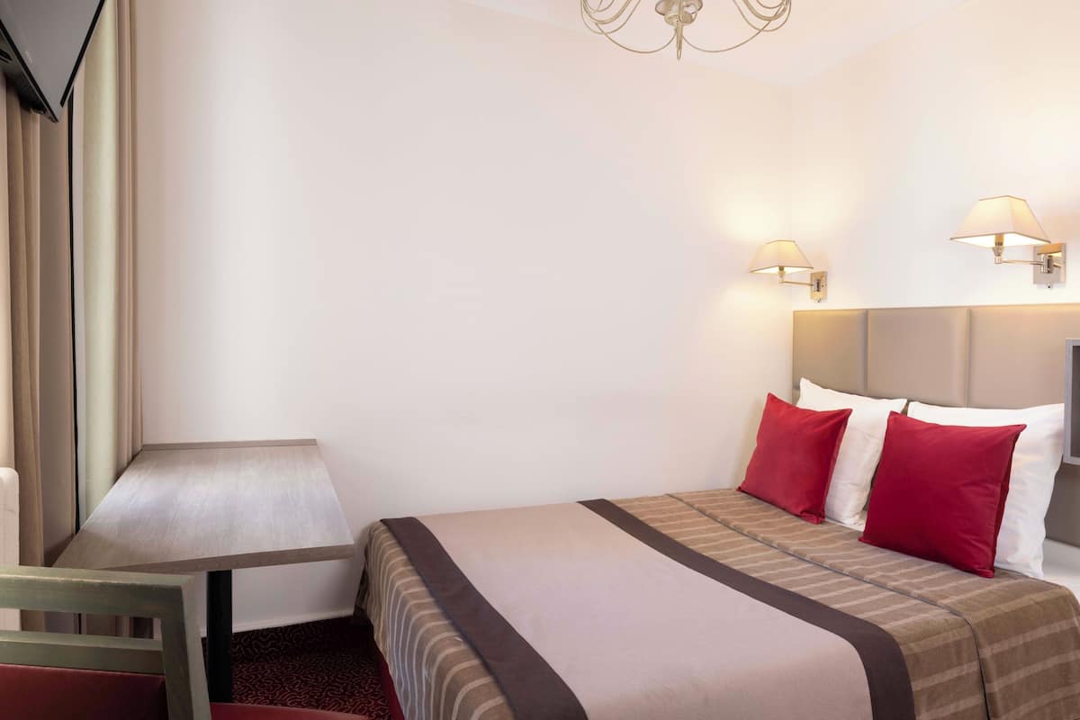 A hotel room with a bed, a small table, and two wall-mounted lamps.