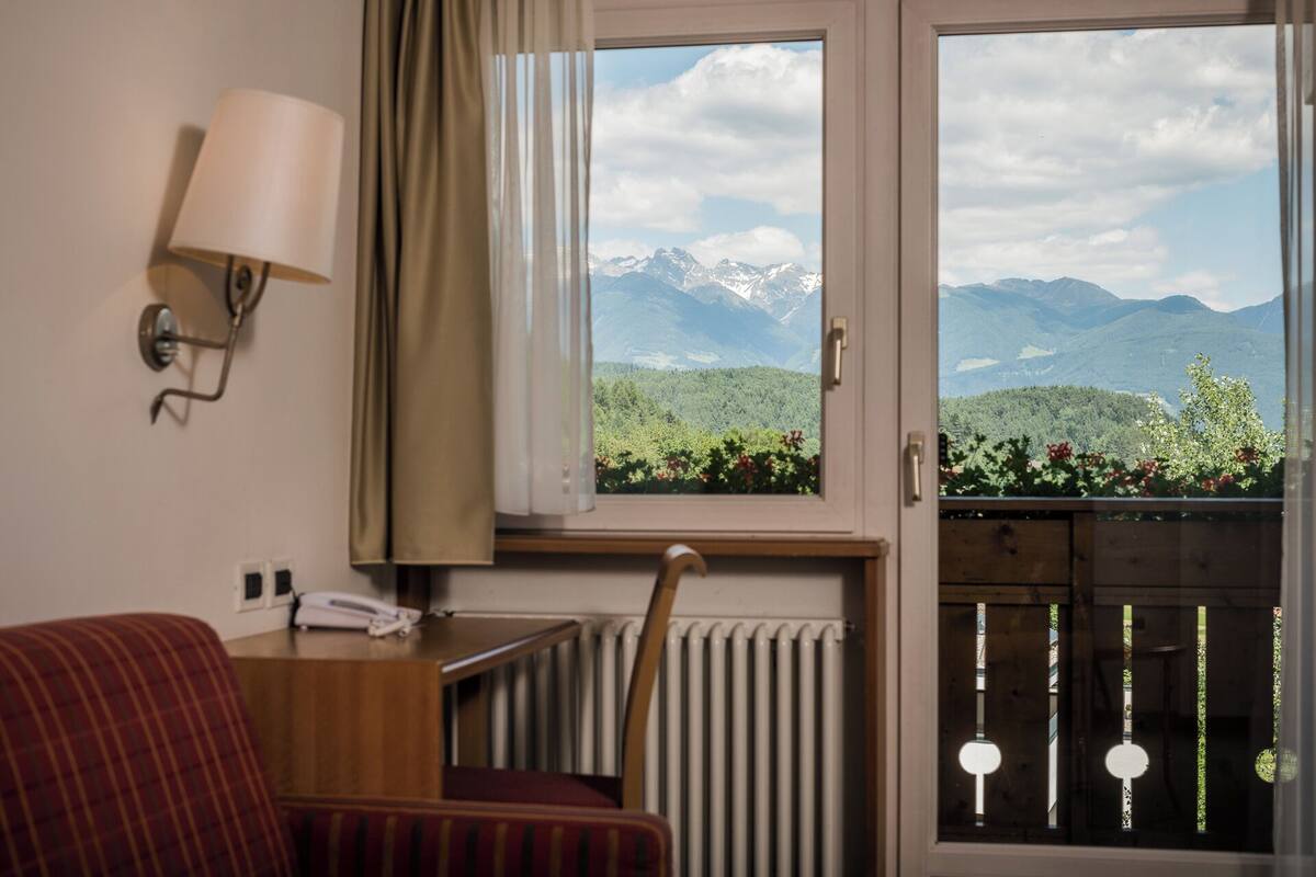 Habitación de hotel con vistas a montañas, un radiador, un teléfono y una ventana con cortinas.