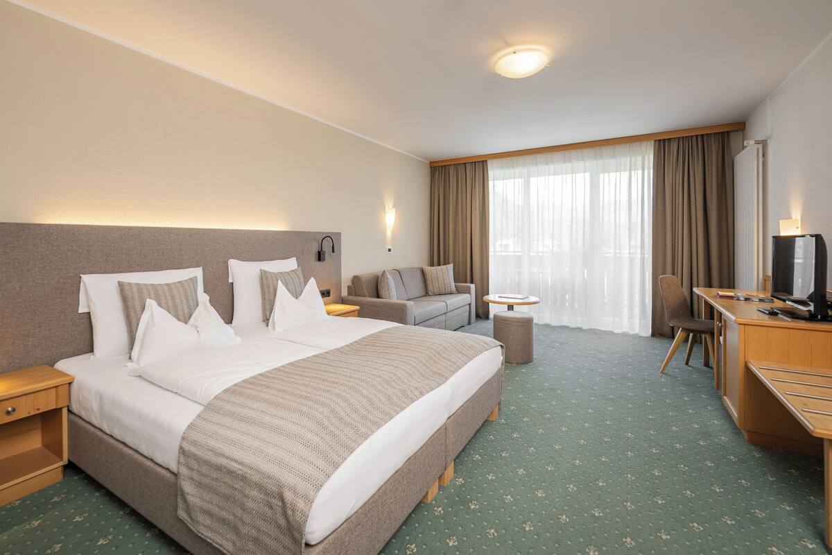 Una habitación de hotel con una cama grande, un escritorio, una silla, un sofá y una televisión.