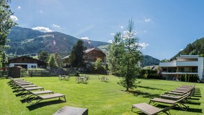Un espace extérieur ensoleillé, aménagé avec des chaises longues disposées en rangées, un petit arbre et des bâtiments en arrière-plan.