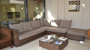 A modern living room with a large L-shaped sectional sofa, a glass coffee table with magazines, and a wicker accent chair. - Mesami Hotel (Durban)