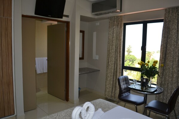 A hotel room with a bed, a TV, a table with chairs, and a window with curtains. - Mesami Hotel (Durban)
