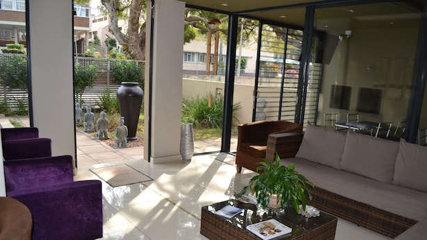 A modern living room with a sofa, armchairs, and a coffee table. There is a large window providing a view of the outside. - Mesami Hotel (Durban)