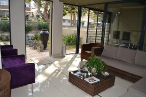 A modern living room with a sofa, armchairs, and a coffee table. There is a large window providing a view of the outside. - Mesami Hotel (Durban)