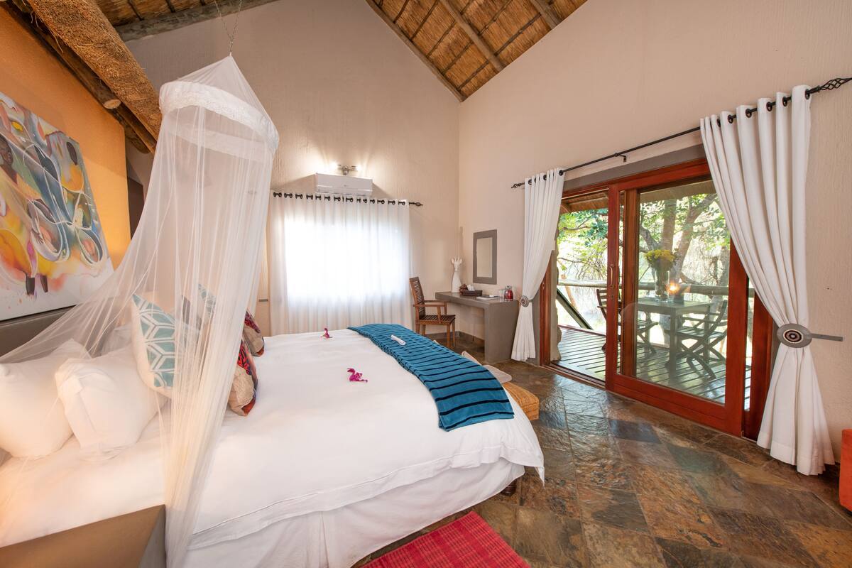 A bedroom with a bed, a desk, a chair, and a view of the outdoors.