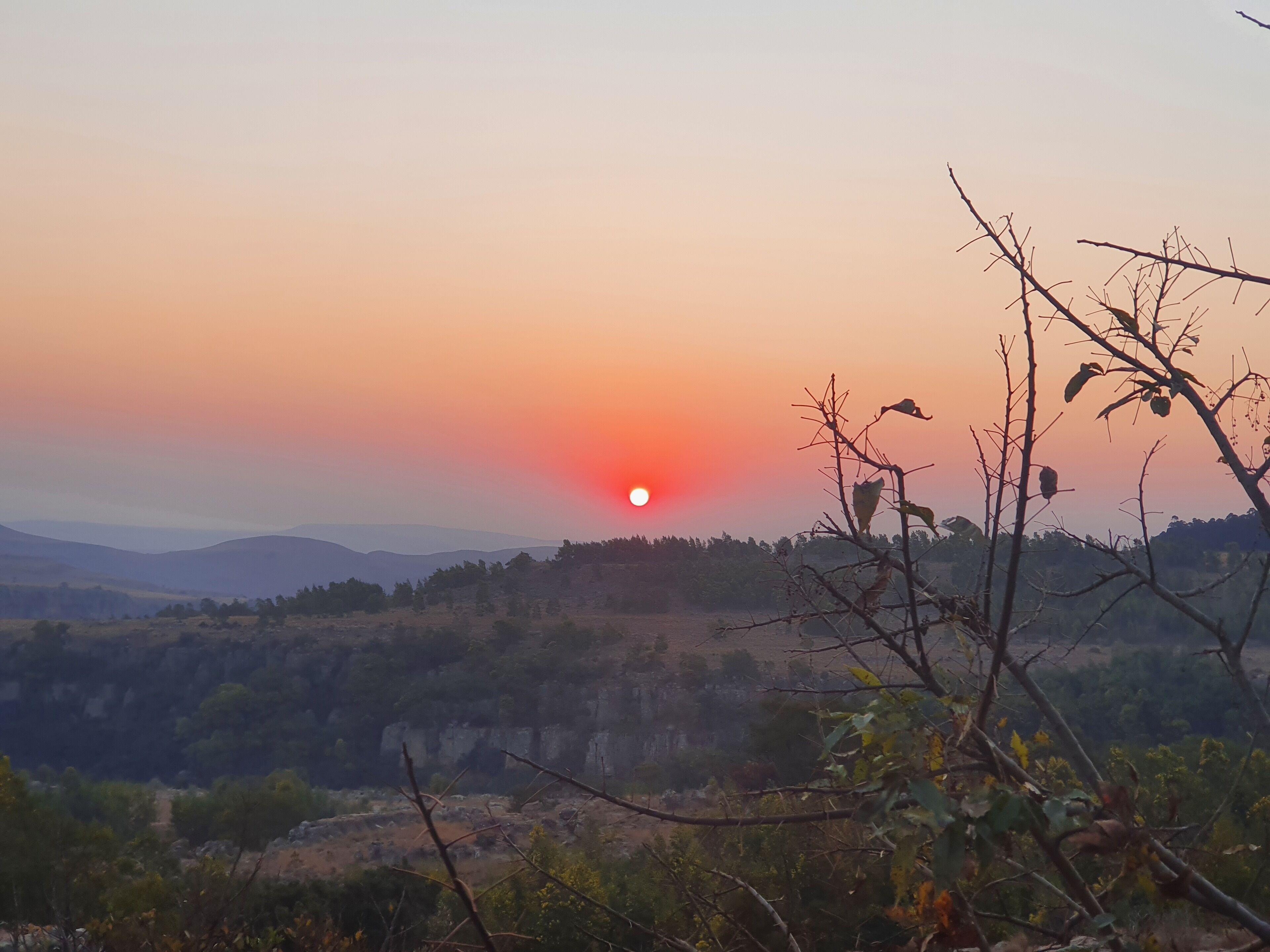 A sunset over a mountainous landscape with a view of the sun setting behind the hills.