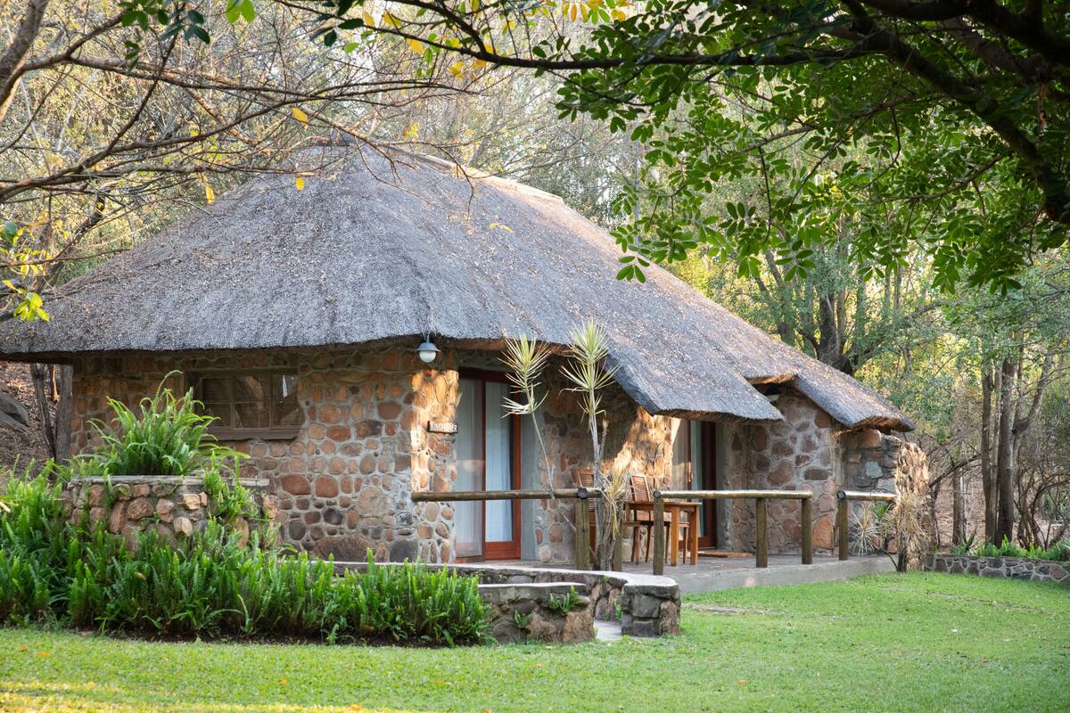 A stone building with a thatched roof, surrounded by greenery and trees.