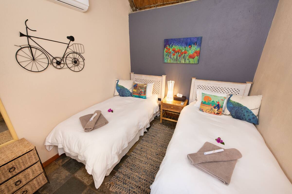 A hotel room with two single beds, a wall-mounted bicycle decoration, a painting, and a nightstand with a lamp.