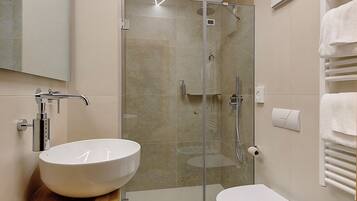 Un baño moderno con ducha acristalada, tocador de madera y lavamanos blanco.