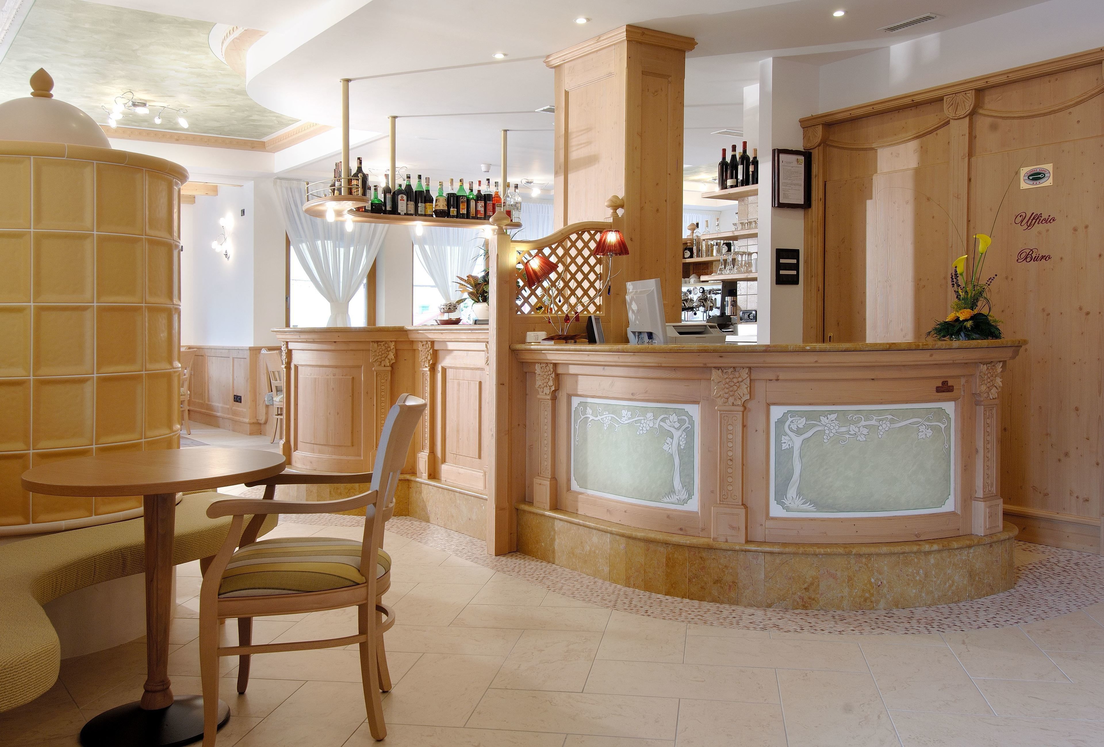 Zona de bar con mostrador de madera, una mesa redonda y una silla. Hay botellas en el mostrador y una planta decorativa a la derecha.
