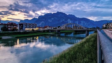 Blick auf einen Fluss mit einer Brücke, Gebäuden und Bergen im Hintergrund.