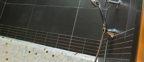A modern bathroom with a glass ceiling, dark tiled walls, and a mosaic-tiled floor.