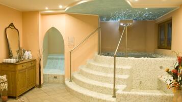 Un espacio de spa con un jacuzzi revestido de mosaicos, un tocador de madera con artículos de aseo y un espejo.