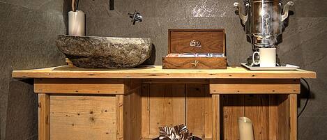 A wooden kitchen with a stone sink, a tea set, and a vase with flowers.