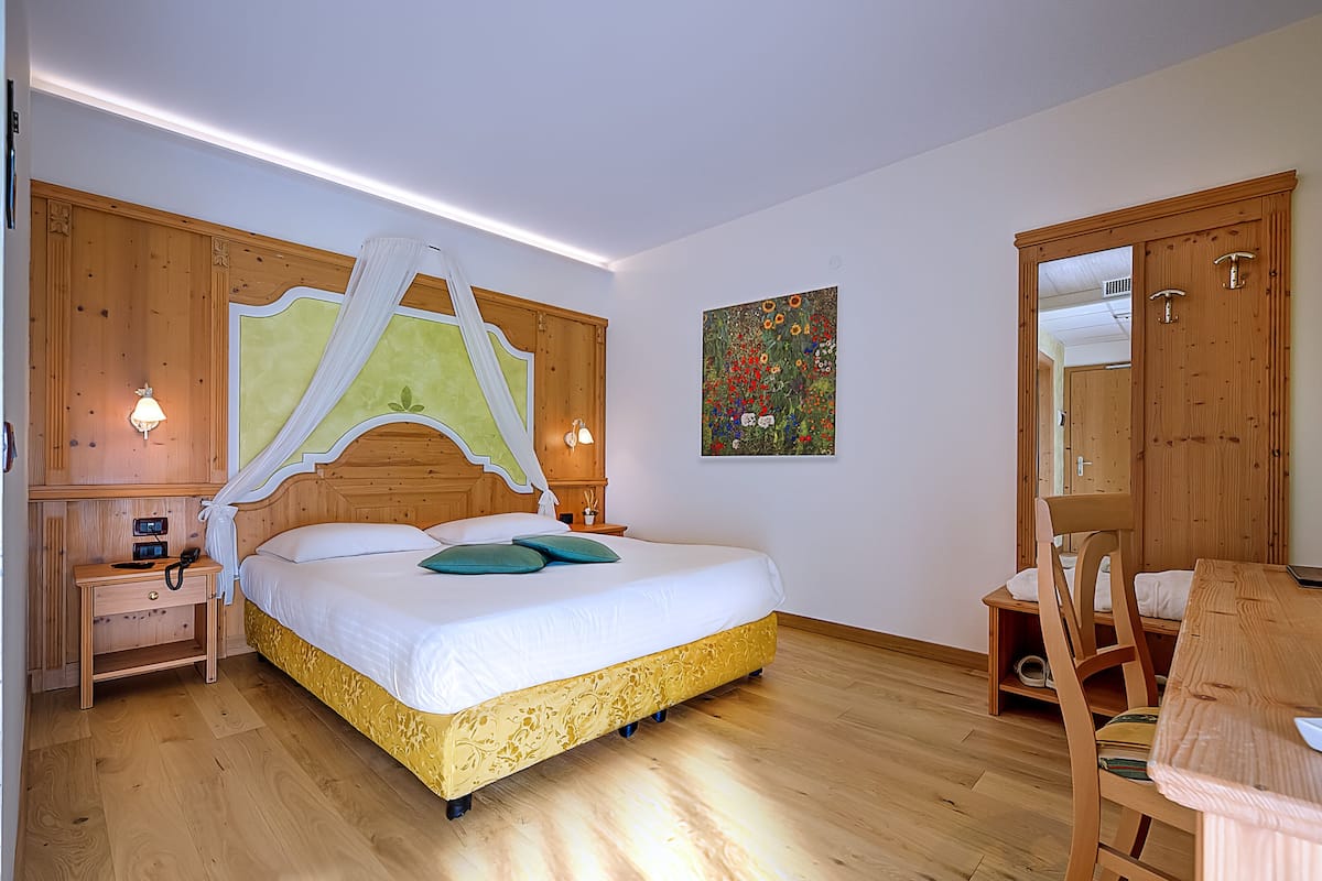 A bedroom with a canopy bed, wooden wardrobe, bedside table with lamp, and a painting on the wall.