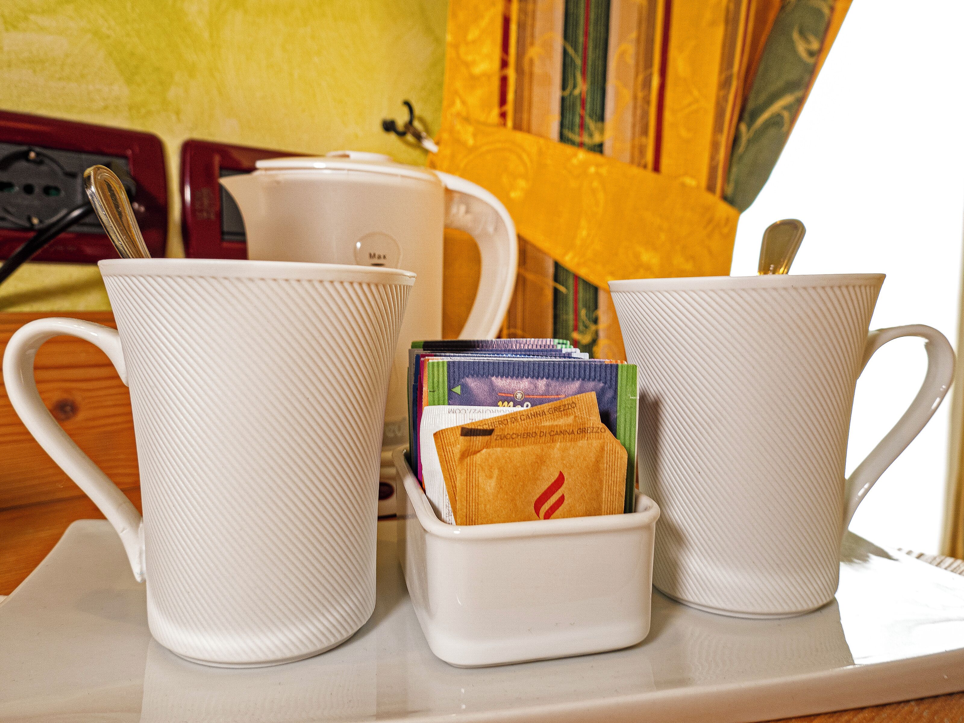 Three white ceramic mugs on a table with a stack of books and a spoon.