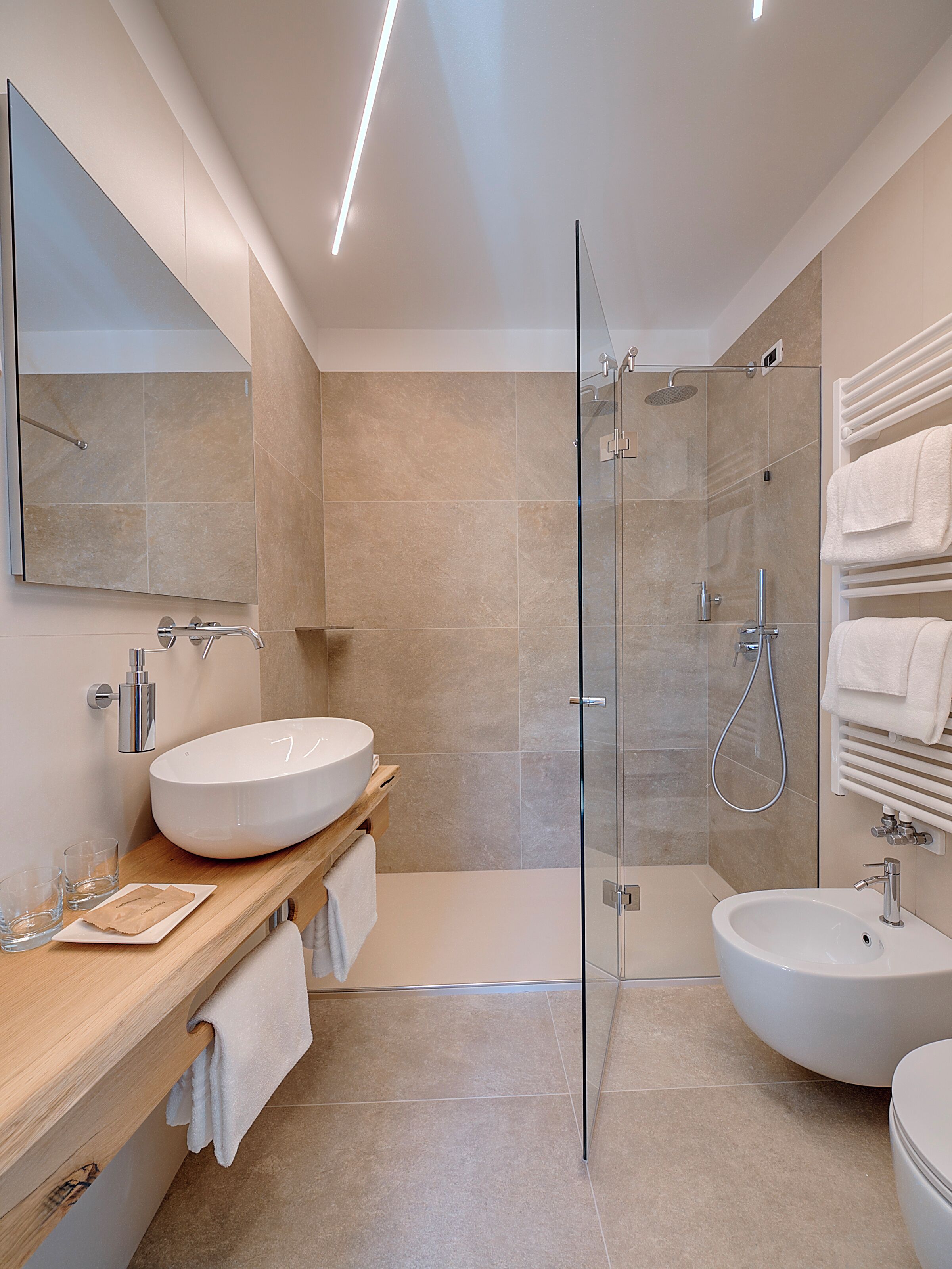 Une salle de bain moderne avec une douche à parois de verre, un grand lavabo blanc et un autre lavabo sur pied, séparé.