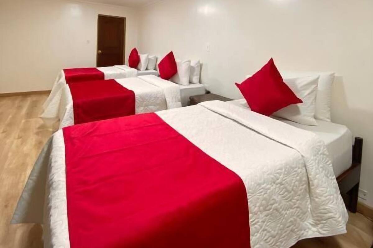 Een hotelkamer met drie bedden, elk voorzien van een witte dekbedovertrek en rode kussens.