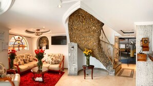 A spacious living area with a sofa set, a coffee table, and a red rug. A stone wall staircase leads to a lower level. - Hotel Fontibon (Bogotá)