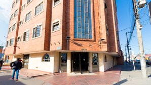 A multi-story building with a brick facade, large windows, and a ground-level entrance with a tiled pavement. - Hotel Fontibon (Bogotá)