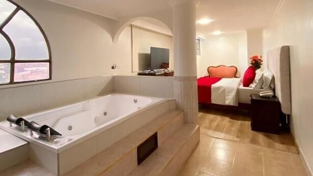 A modern bathroom with a large bathtub, a vanity with a mirror, and a window. - Hotel Fontibon (Bogotá)