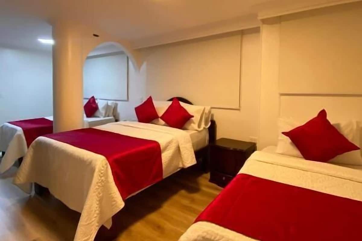 Een hotelkamer met drie bedden, elk met rood-wit beddengoed, en een houten vloer.