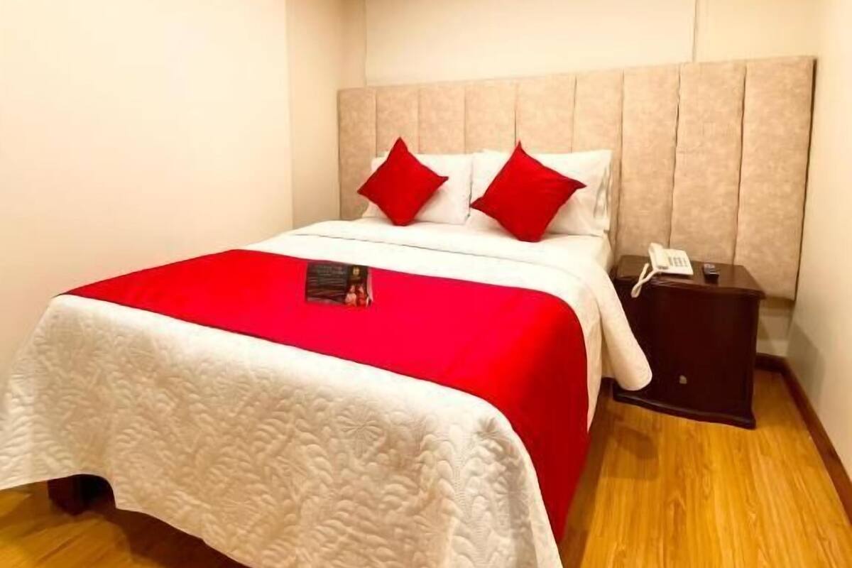 Hotelkamer met een groot bed, een hoofdeinde, een nachtkastje met een telefoon en een houten vloer.