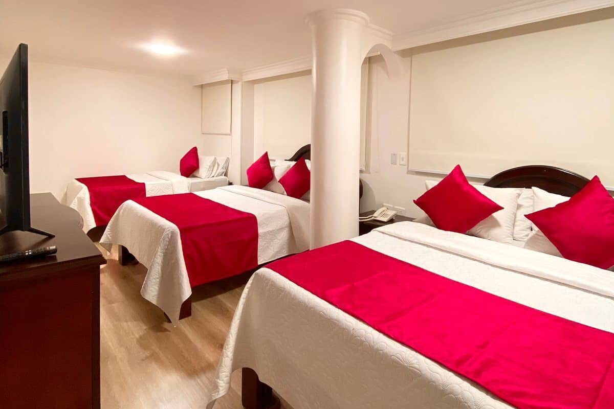 Hotelkamer met twee bedden, elk met witte lakens en rode kussens. Er staat een televisie op een houten dressoir en een telefoon op het nachtkastje.