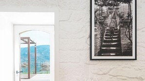 Un comedor con una mesa dispuesta para dos personas, una fotografía blanco y negro enmarcada en la pared y una puerta que da a un espacio exterior con vistas al paisaje.
