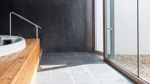 Un baño moderno con tocador de madera, una bañera grande y una pared revestida de baldosas oscuras.