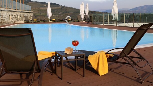 Zona junto a la piscina con sillones de descanso, una mesa con una bebida y una caja, y sombrillas.