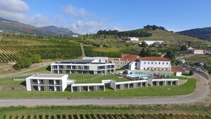 Un edificio moderno con un patio central, rodeado de viñedos y terreno montañoso.