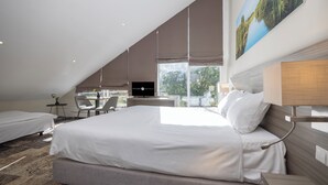 A modern hotel room with a large bed, a desk, and a chair. There is a painting on the wall and a window providing a view of the outdoors.