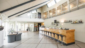 A spacious lobby with a high ceiling, a central bar area with stools, and a staircase leading to an upper level.