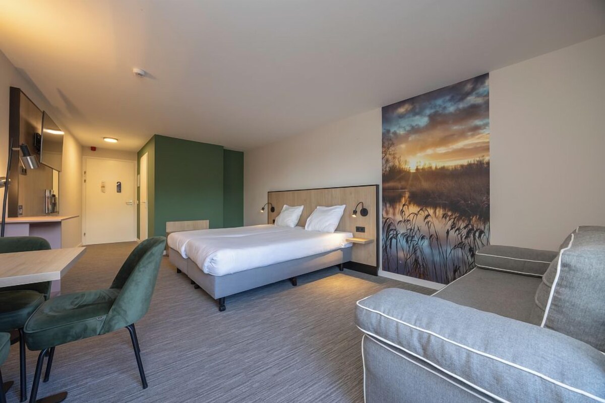 A hotel room with a bed, a desk, a chair, a couch, and a painting on the wall.