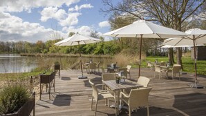An outdoor deck with wicker furniture and white umbrellas, overlooking a body of water.