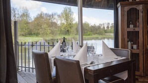 A dining area with tables set for two, overlooking a body of water and trees.