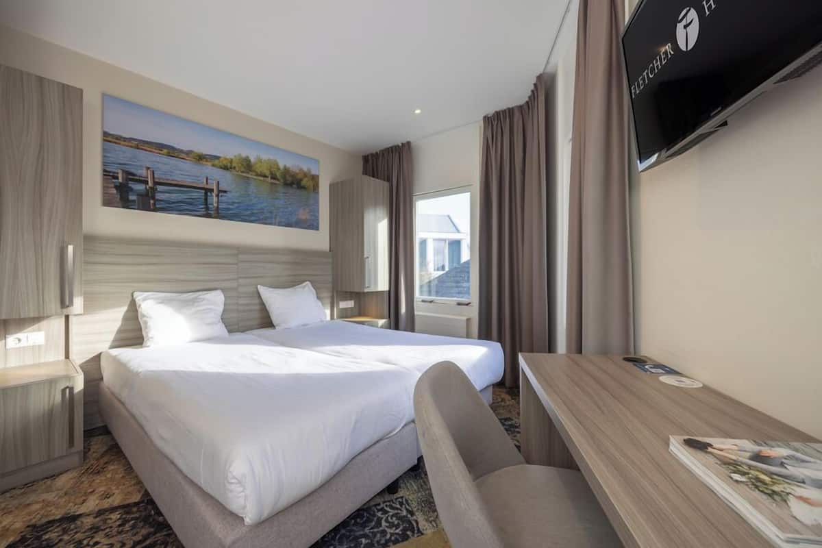 Quarto de hotel com uma cama grande, uma escrivaninha, uma televisão e um quadro de um lago.