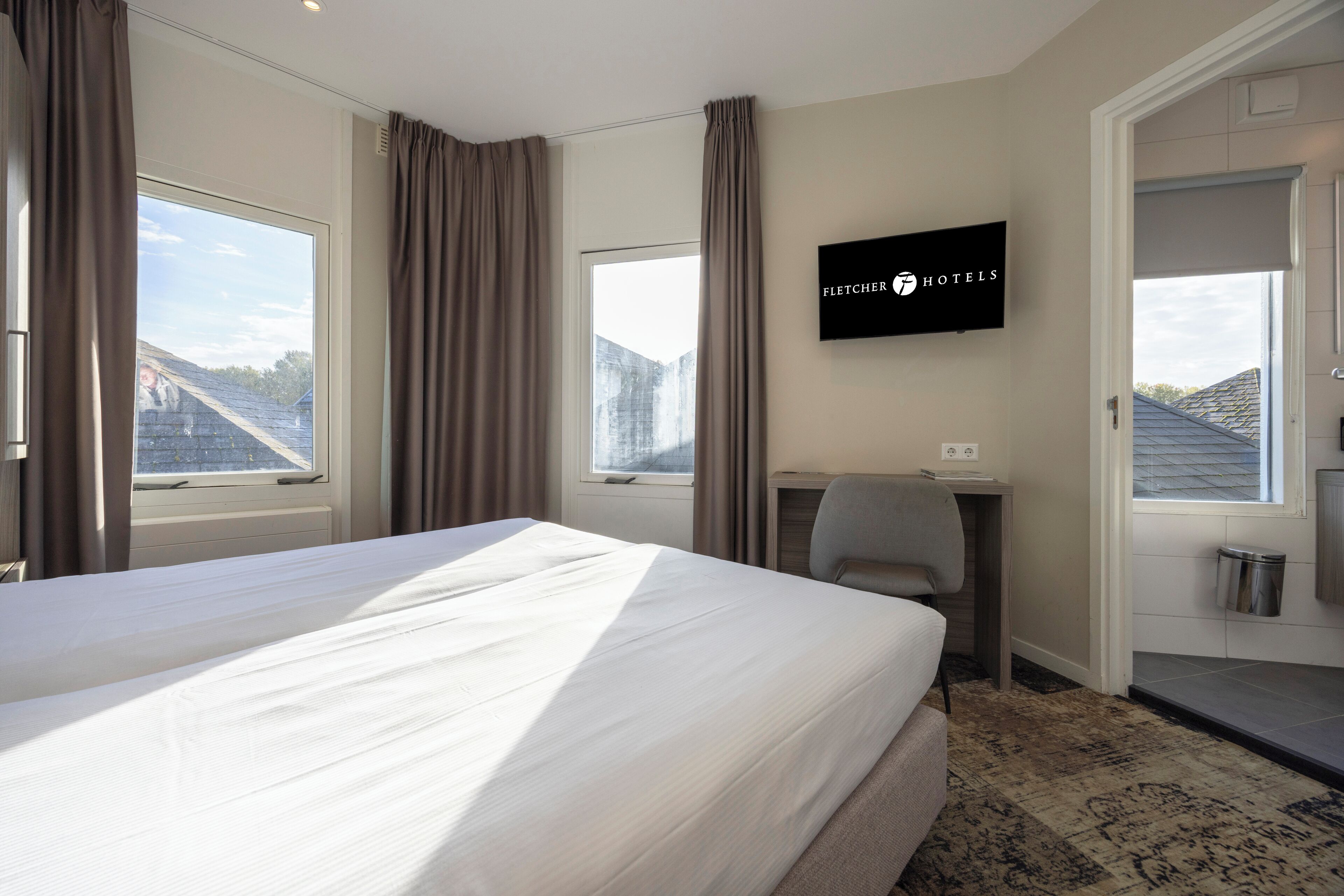 A hotel room with a large bed, a desk, a television, and a view of the outside.