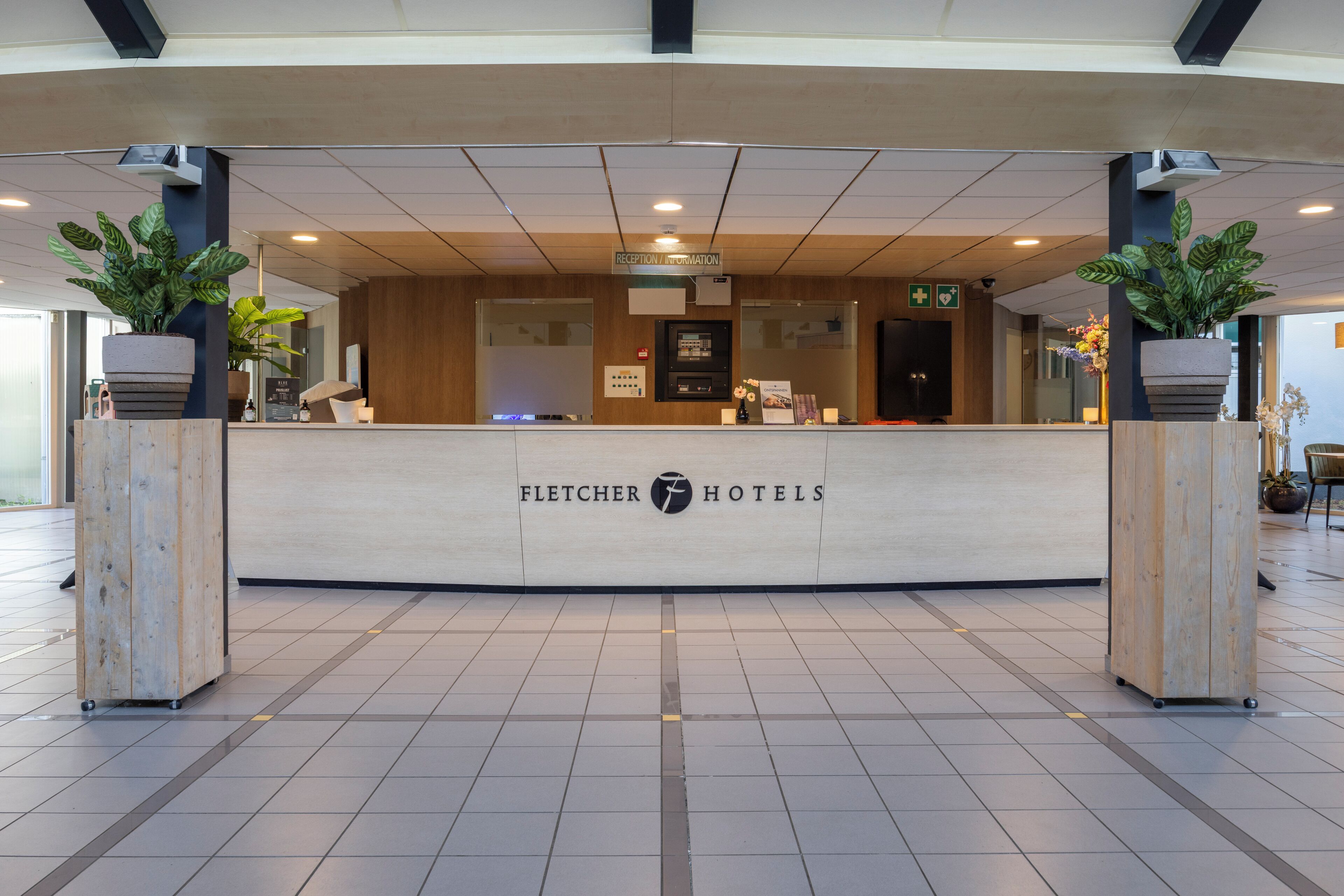 Mostrador de recepción en Fletcher Hotels, con un diseño moderno, un quiosco de información digital y plantas en macetas.