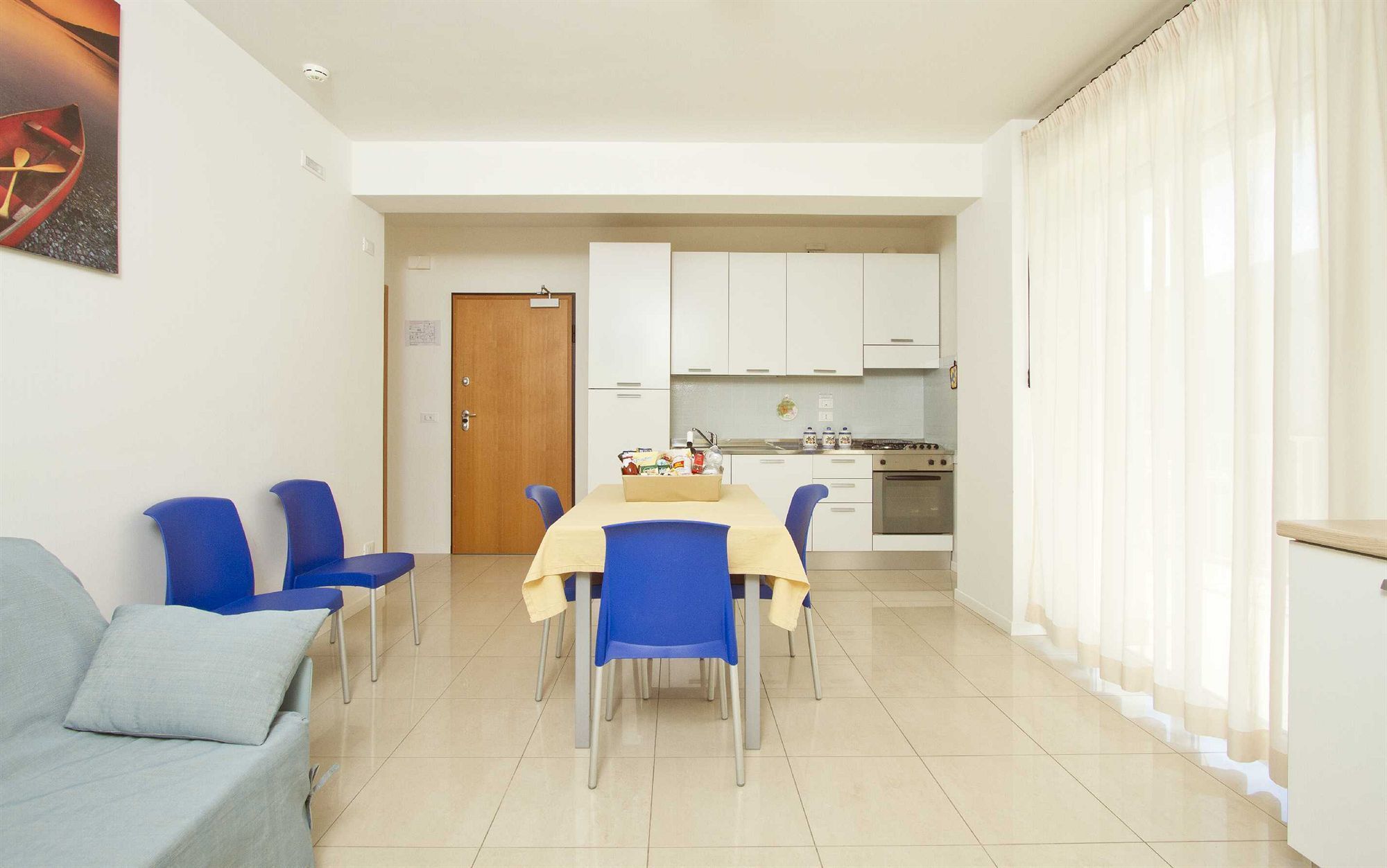 Een ruimtelijk ingerichte leefruimte met een eethoek, kitchenette en een deur naar een andere kamer.