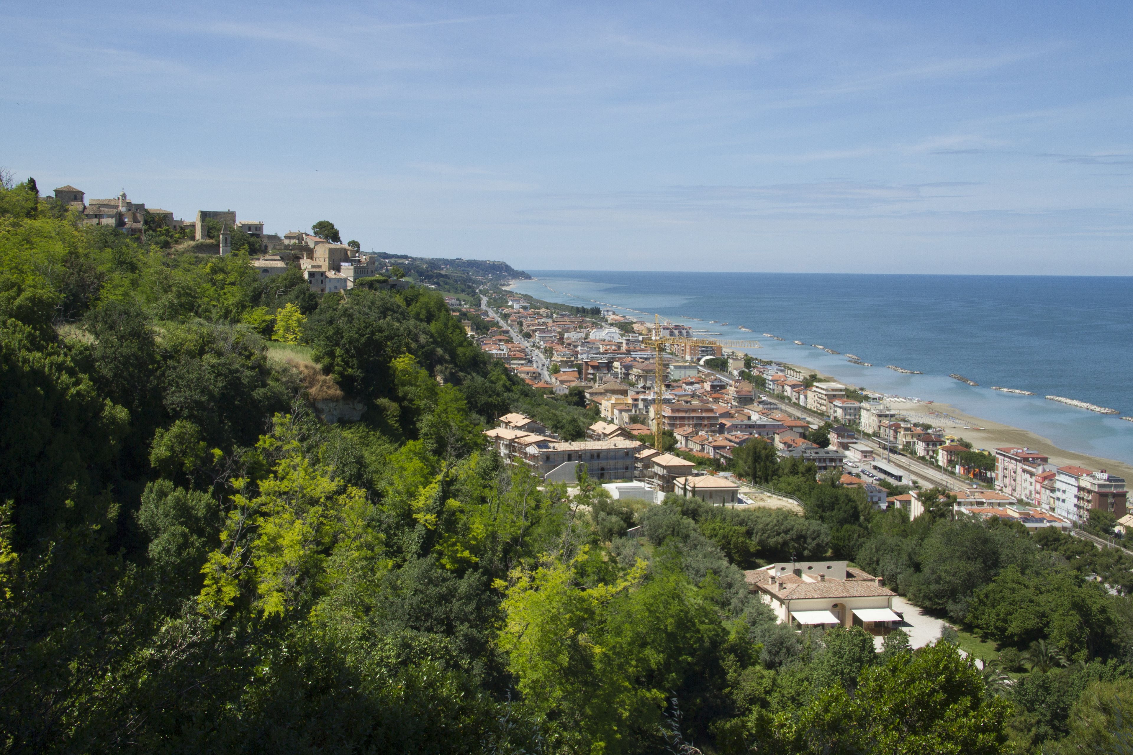 A coastal town with buildings along the beach and a hillside with dense greenery.