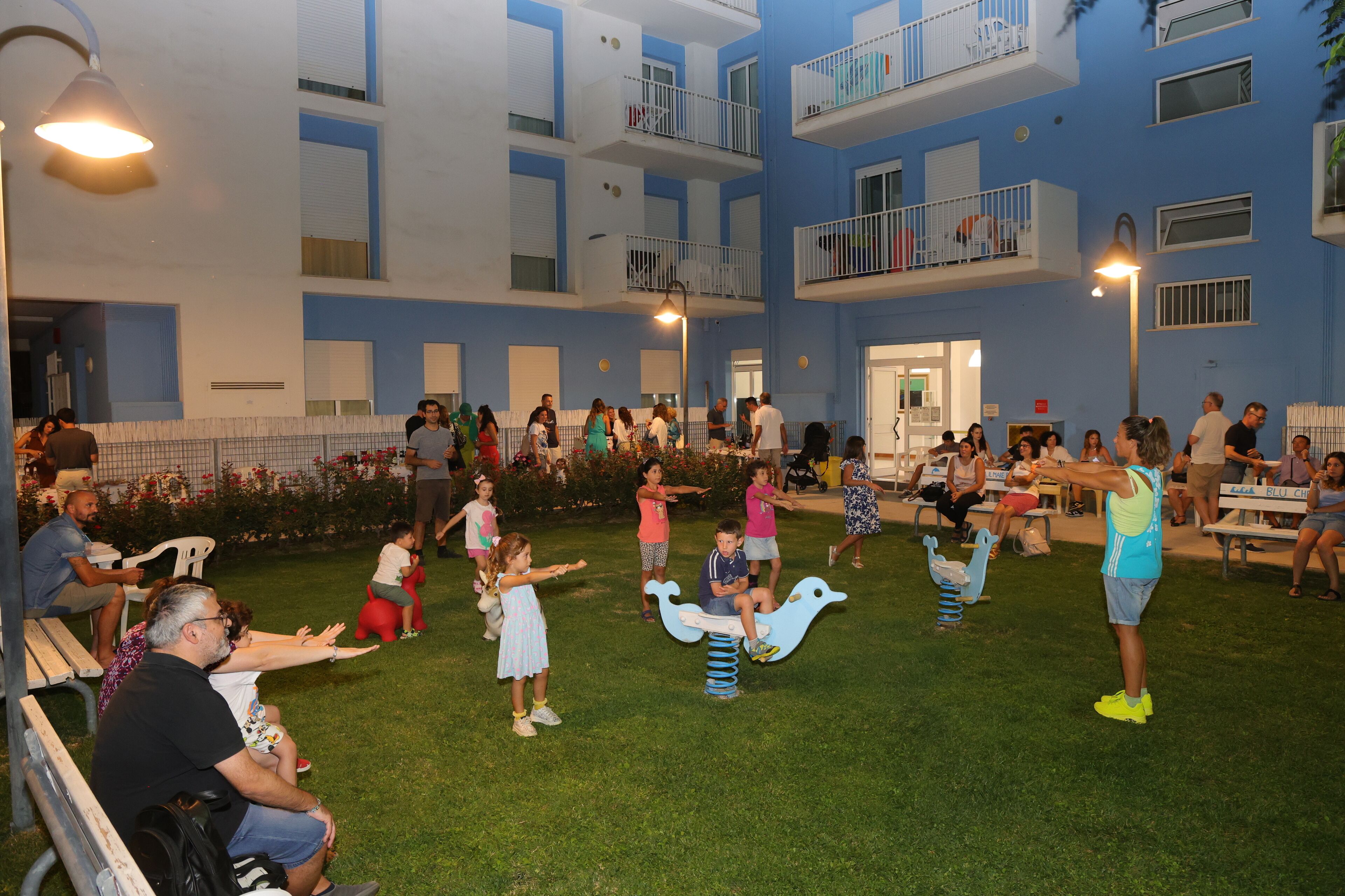 Un patio exterior con un parque infantil, zonas de estar y un edificio con balcones.