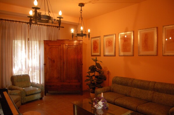 Una sala de estar con un mueble de madera, un sofá, una silla, un piano y una araña.
