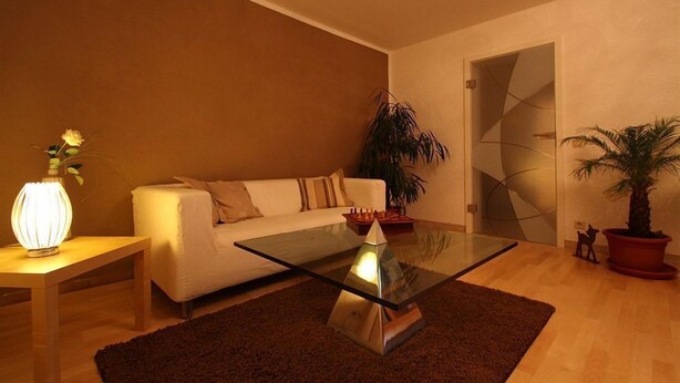 Un salon moderne avec une table basse en verre, un canapé blanc et un tapis marron foncé.
