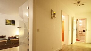 Un intérieur moderne avec une cloison en verre, une petite table sur laquelle est posé un modèle de bateau, un luminaire fixé au mur et un ventilateur de plafond.